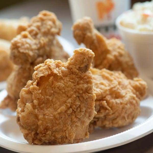 Crispy fried chicken pieces on a white plate, with sides in the blurred background.
