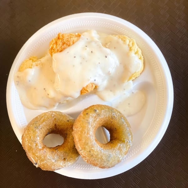 Connie's Chicken fried chicken with gravy and two glazed donuts on a white plate.