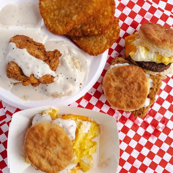 Connie's Chicken fried chicken, biscuits with gravy, hash browns, and breakfast sandwiches on a red checkered tablecloth.