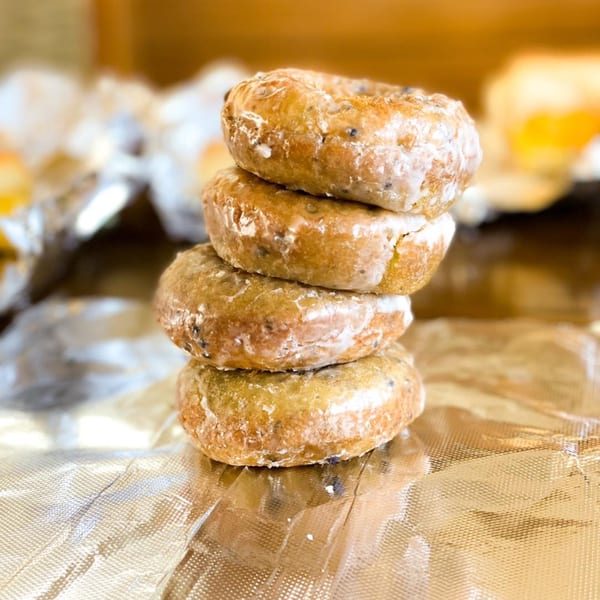 Stack of four glazed donuts with dark specks, resting on crinkled foil.