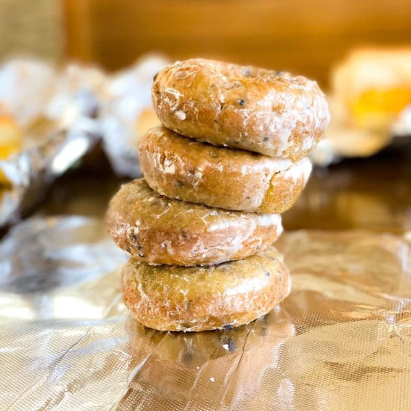 A stack of four glazed blueberry donuts on crinkled foil, with a warm, blurred background.