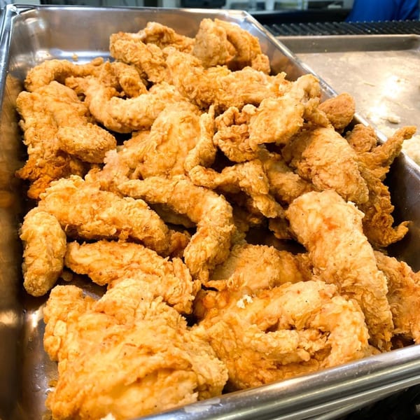 A metal tray filled with numerous golden-brown, crispy fried chicken tenders.