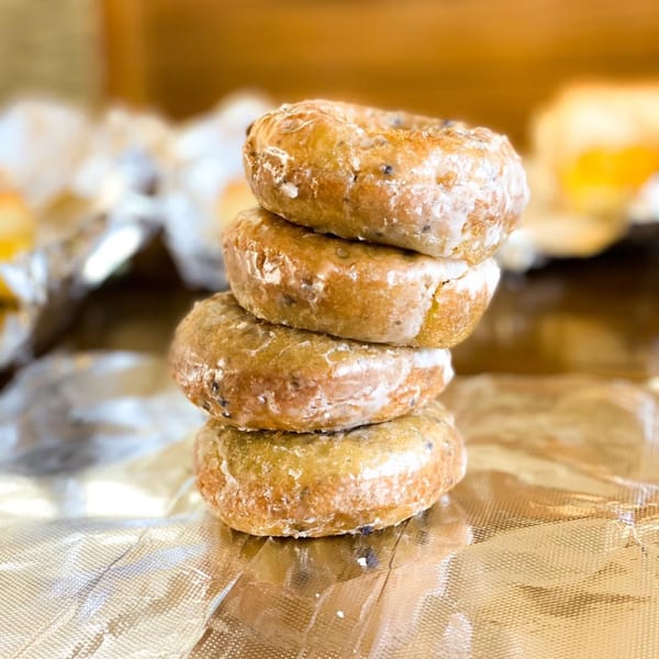 A stack of four glazed donuts with dark specks, resting on crinkled foil.