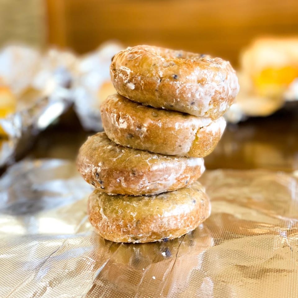A stack of four glazed donuts with dark specks, resting on crinkled foil.