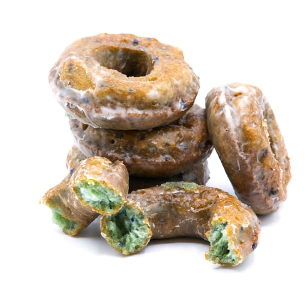 A pile of glazed donuts with green interiors and blue specks, one broken in half.