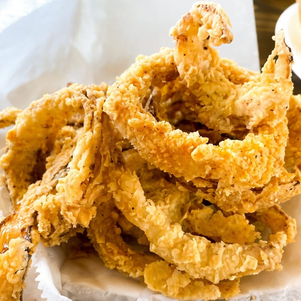 Close-up of crispy, golden-brown fried onion rings in a white paper-lined basket at Connie's Chicken.